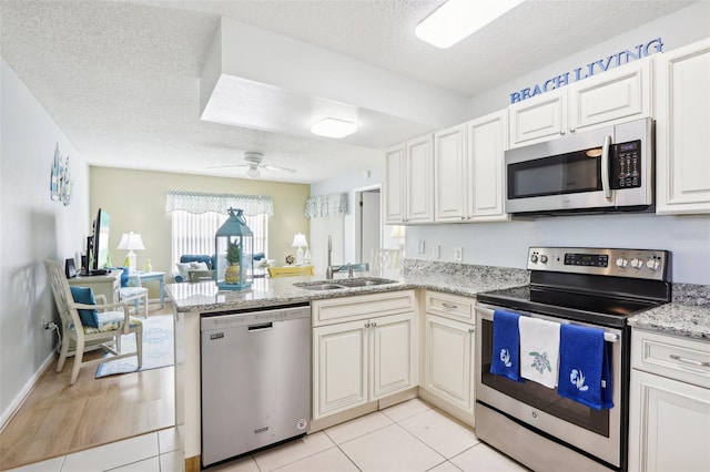 kitchen with kitchen peninsula, sink, appliances with stainless steel finishes, a textured ceiling, and light hardwood / wood-style floors