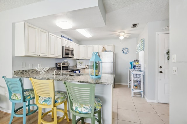 kitchen featuring kitchen peninsula, stainless steel appliances, light stone countertops, white cabinets, and ceiling fan