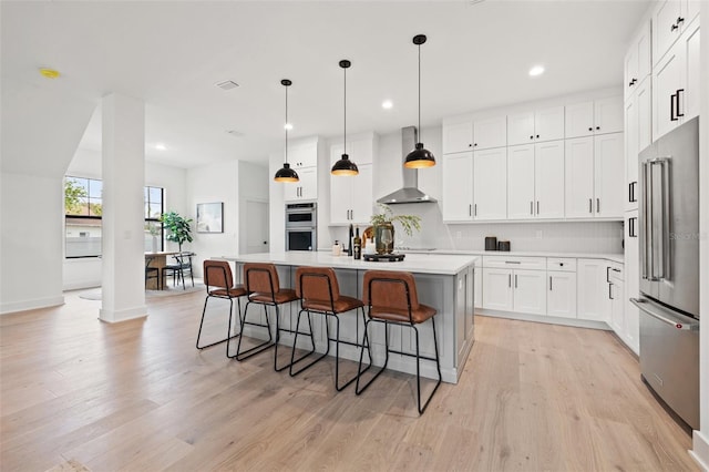 kitchen featuring appliances with stainless steel finishes, light wood-style flooring, wall chimney range hood, and a breakfast bar