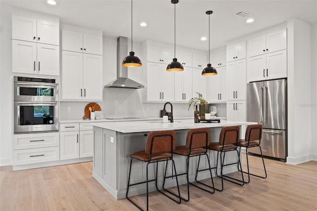 kitchen with appliances with stainless steel finishes, light countertops, wall chimney range hood, and white cabinetry