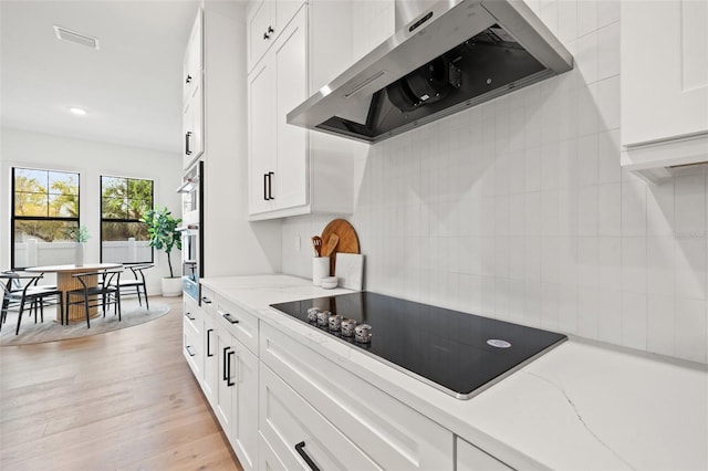 kitchen featuring black electric stovetop, light wood-style floors, white cabinetry, stainless steel oven, and wall chimney exhaust hood