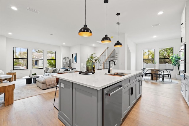 kitchen featuring a center island with sink, stainless steel appliances, gray cabinets, light wood-type flooring, and a sink