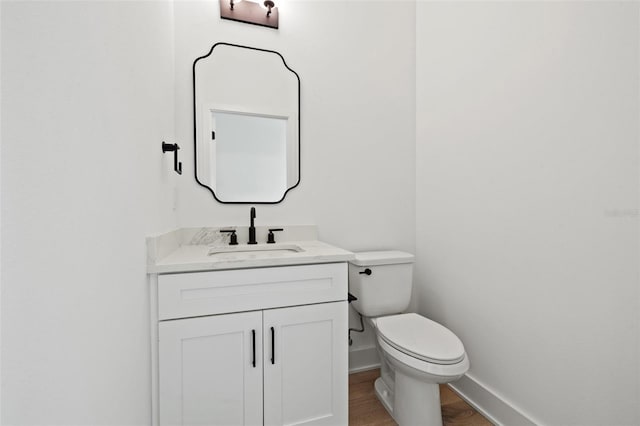 half bath featuring toilet, wood finished floors, vanity, and baseboards