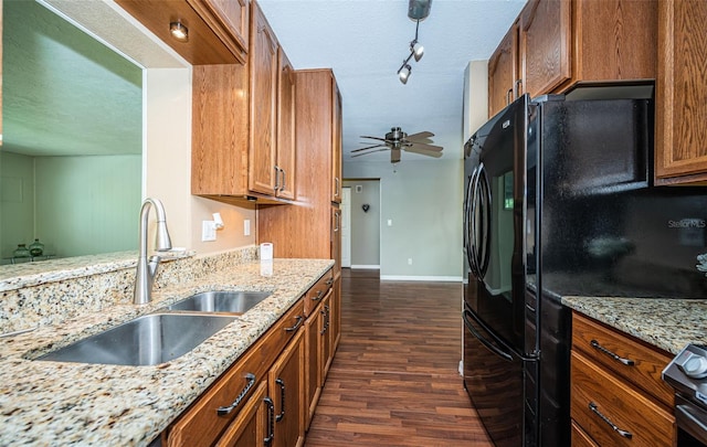 kitchen with sink, dark wood-type flooring, black fridge, light stone counters, and stainless steel stove