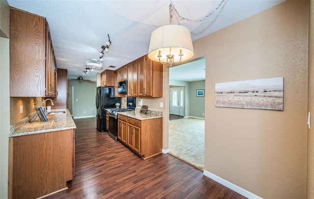 kitchen featuring pendant lighting, dark wood-type flooring, black appliances, sink, and light stone countertops