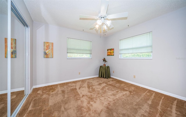 empty room with a textured ceiling, carpet floors, ceiling fan, and a healthy amount of sunlight