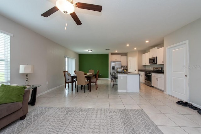 kitchen with ceiling fan, stainless steel appliances, a breakfast bar area, a kitchen island with sink, and white cabinets