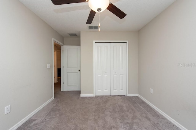 unfurnished bedroom with a textured ceiling, a closet, ceiling fan, and light colored carpet