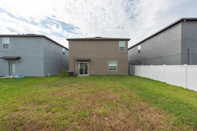 rear view of house featuring central AC unit and a lawn