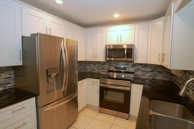 kitchen featuring tasteful backsplash, stainless steel appliances, sink, light tile patterned floors, and white cabinets