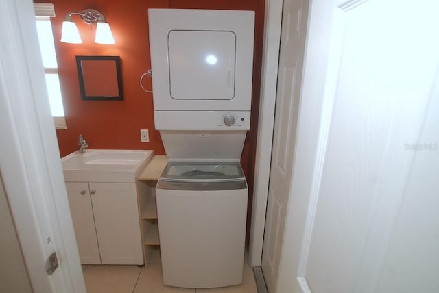 washroom with light tile patterned floors, stacked washer and clothes dryer, and sink