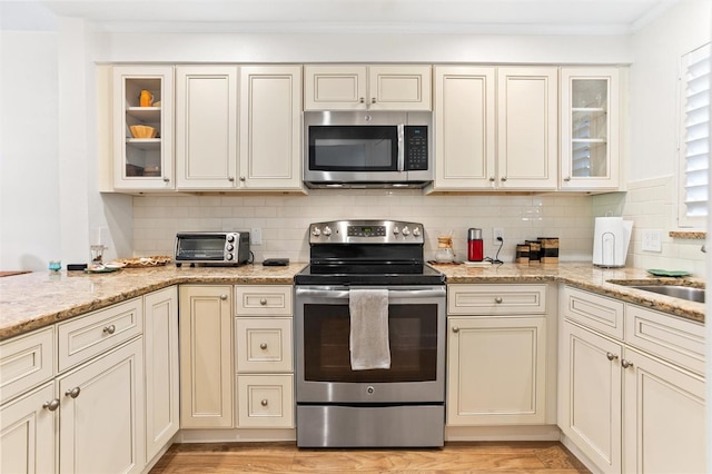 kitchen with backsplash, light stone countertops, stainless steel appliances, and cream cabinets