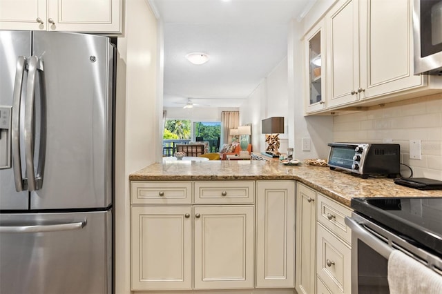 kitchen with cream cabinets, backsplash, ceiling fan, stainless steel appliances, and light stone counters