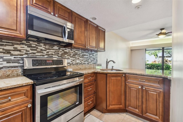 kitchen with appliances with stainless steel finishes, sink, light stone counters, and light tile patterned floors