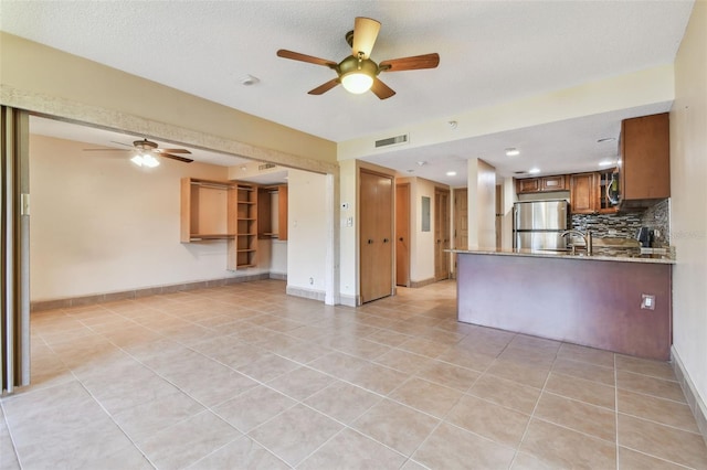 kitchen with appliances with stainless steel finishes, kitchen peninsula, a textured ceiling, and light tile patterned flooring