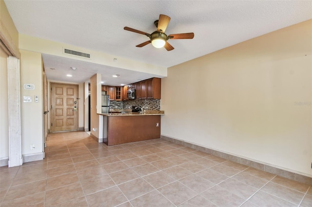 kitchen with a textured ceiling, decorative backsplash, light tile patterned floors, and kitchen peninsula