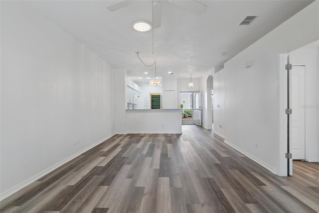 unfurnished living room featuring arched walkways, dark wood-type flooring, visible vents, and a ceiling fan