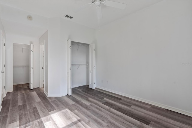 unfurnished bedroom featuring baseboards, visible vents, ceiling fan, wood finished floors, and multiple closets