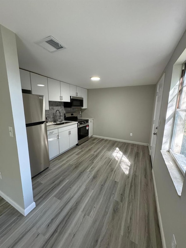 kitchen with decorative backsplash, white cabinetry, light wood-type flooring, sink, and stainless steel appliances