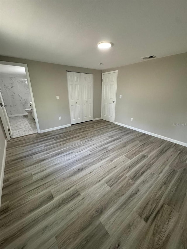 unfurnished bedroom with a closet, hardwood / wood-style floors, and ensuite bath