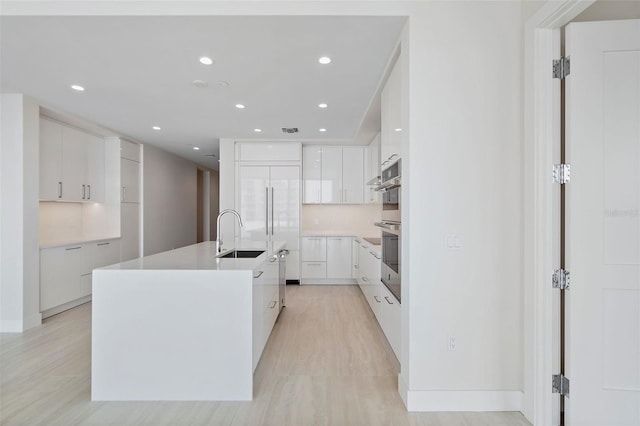 kitchen with white cabinetry, sink, light hardwood / wood-style flooring, paneled built in fridge, and a kitchen island with sink