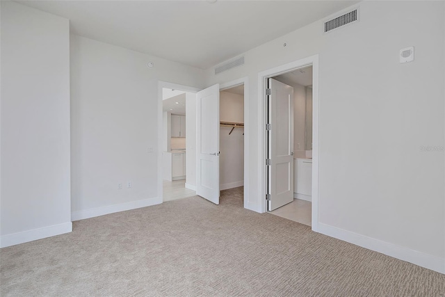 unfurnished bedroom with a walk in closet, a closet, ensuite bath, and light colored carpet