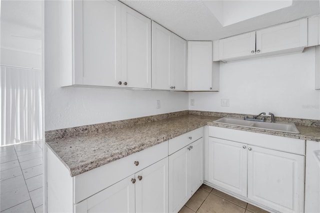 kitchen with white cabinets, sink, light stone countertops, light tile patterned floors, and a textured ceiling