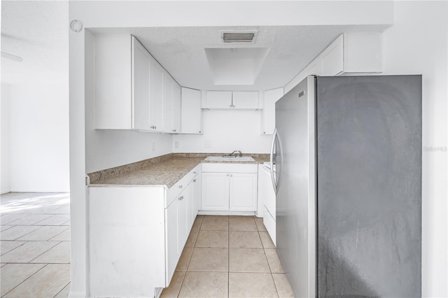 kitchen with a textured ceiling, sink, white cabinets, stainless steel refrigerator, and light tile patterned flooring