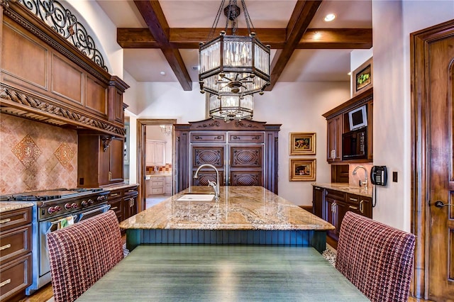 kitchen with decorative backsplash, high end stove, an island with sink, a notable chandelier, and sink