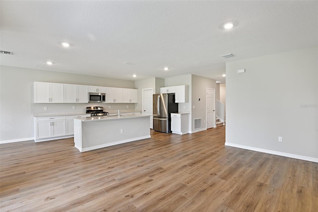 kitchen featuring white cabinets, a textured ceiling, a kitchen island with sink, light wood-type flooring, and stainless steel appliances