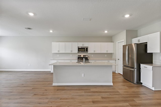 kitchen with appliances with stainless steel finishes, a textured ceiling, white cabinets, light hardwood / wood-style flooring, and a center island with sink