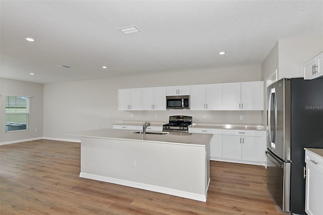 kitchen with appliances with stainless steel finishes, light wood-type flooring, and a center island with sink