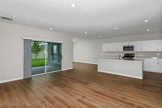 kitchen with a textured ceiling, hardwood / wood-style floors, white cabinetry, black gas range oven, and a kitchen island with sink