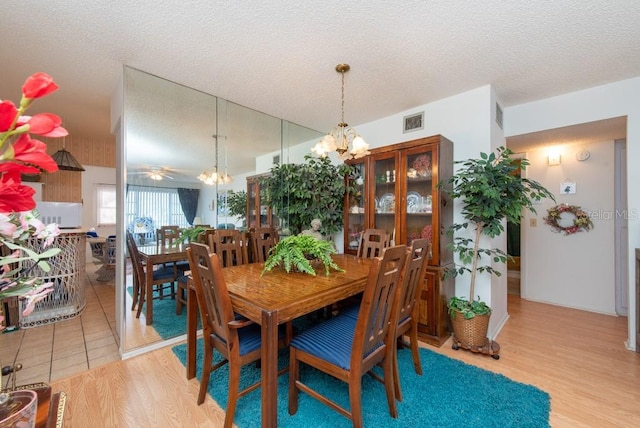 dining space featuring light hardwood / wood-style flooring, a textured ceiling, and ceiling fan with notable chandelier