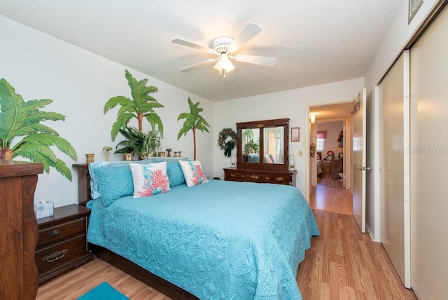 bedroom with light hardwood / wood-style flooring, a textured ceiling, a closet, and ceiling fan