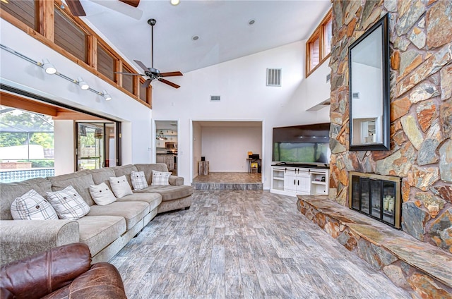 living room featuring hardwood / wood-style flooring, ceiling fan, a stone fireplace, and high vaulted ceiling