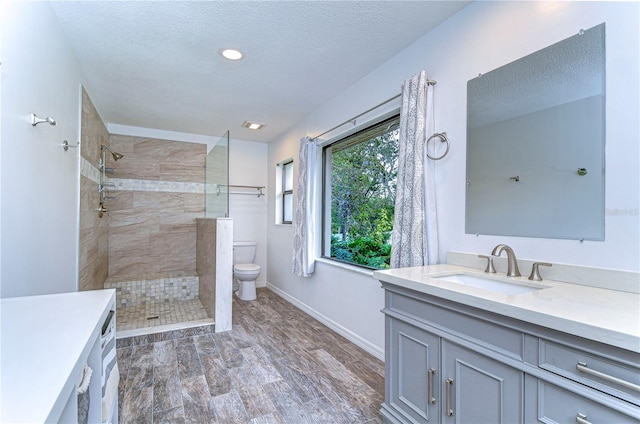 bathroom with tiled shower, vanity, hardwood / wood-style flooring, and toilet