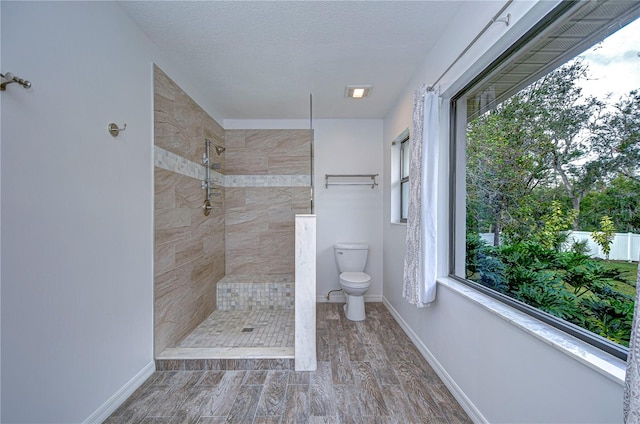 bathroom with hardwood / wood-style floors, tiled shower, a textured ceiling, and toilet