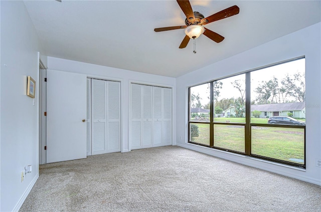 unfurnished bedroom featuring multiple closets, light colored carpet, and ceiling fan