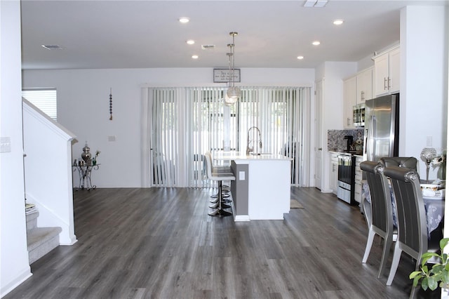 kitchen featuring appliances with stainless steel finishes, an island with sink, a kitchen bar, white cabinetry, and pendant lighting