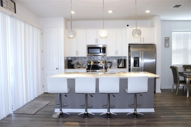 kitchen with appliances with stainless steel finishes, an island with sink, white cabinetry, pendant lighting, and dark wood-type flooring