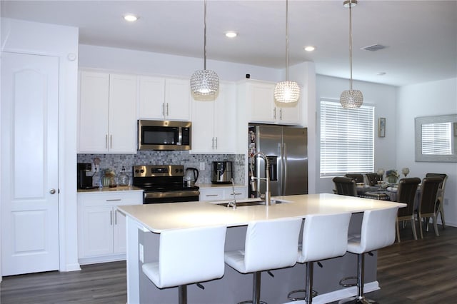 kitchen featuring white cabinetry, stainless steel appliances, a kitchen island with sink, and hanging light fixtures