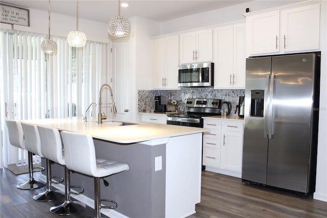 kitchen featuring appliances with stainless steel finishes, white cabinetry, hanging light fixtures, and a center island with sink