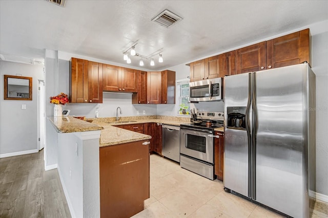 kitchen featuring kitchen peninsula, appliances with stainless steel finishes, light stone countertops, sink, and light hardwood / wood-style flooring