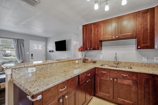 kitchen featuring a textured ceiling, kitchen peninsula, light stone countertops, and sink