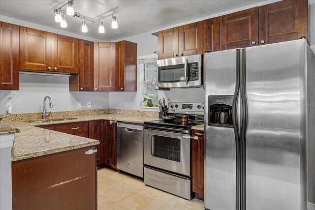 kitchen with rail lighting, sink, light tile patterned floors, light stone counters, and stainless steel appliances