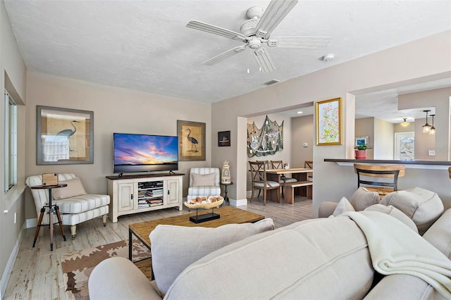 living room with light wood-type flooring, ceiling fan, and a textured ceiling