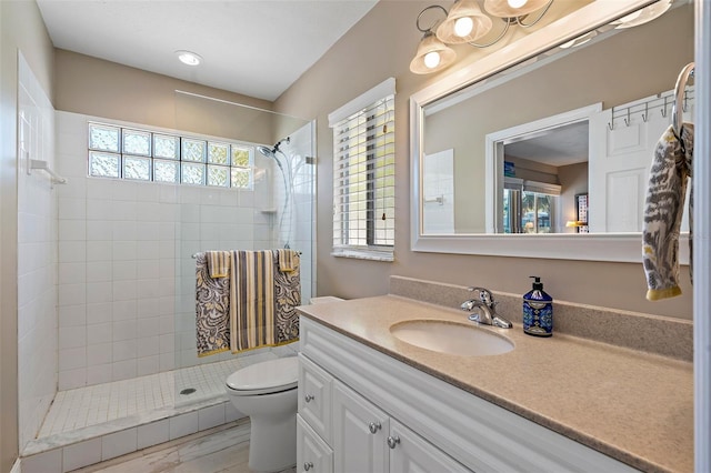 bathroom featuring toilet, tiled shower, and vanity