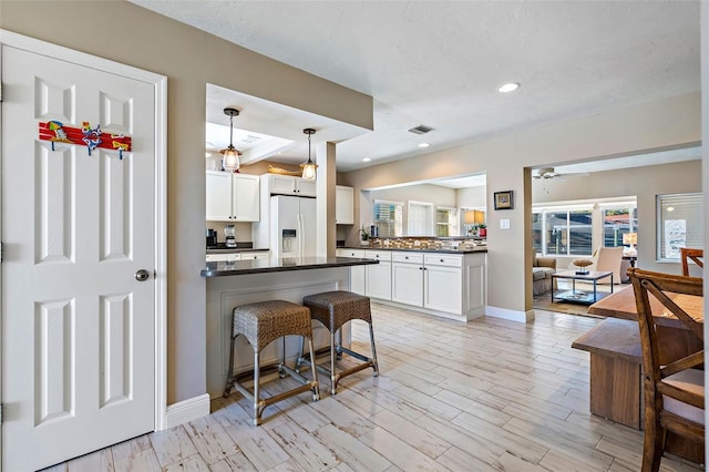 kitchen featuring white refrigerator with ice dispenser, a breakfast bar, pendant lighting, and white cabinetry