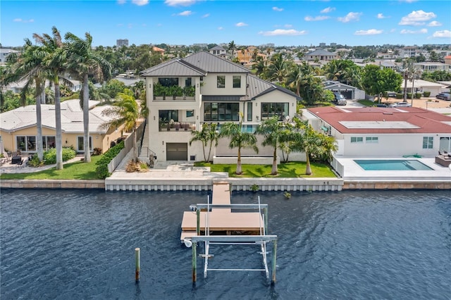 back of house with an in ground hot tub, a balcony, and a water view